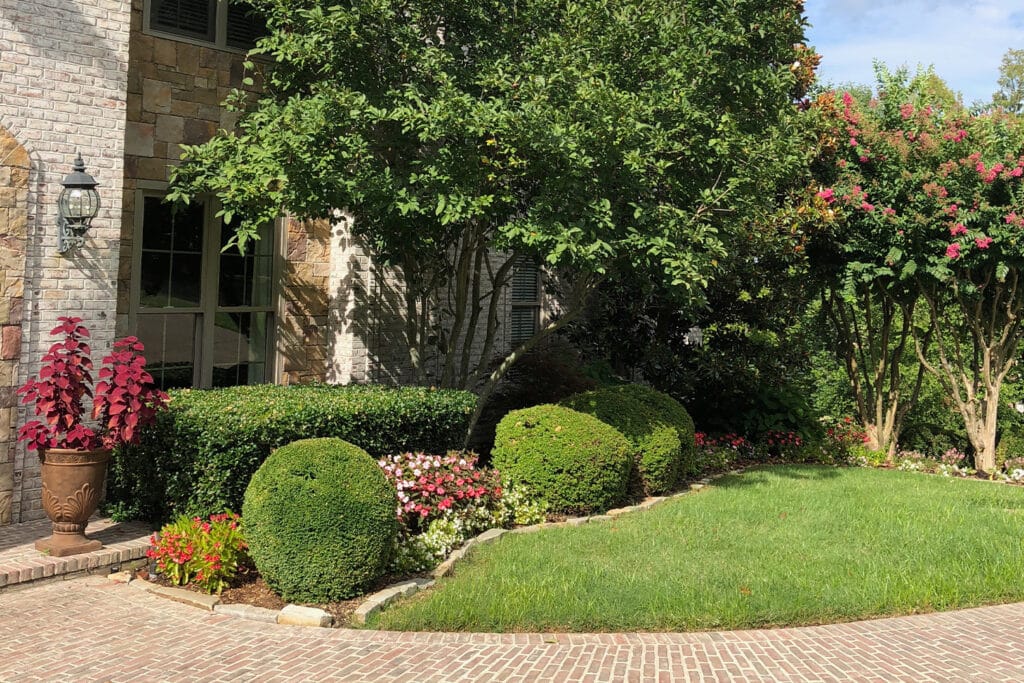 a close up of a flower garden in front of a brick building, the landscape was installed by Opportunity Landscapes and Nursery